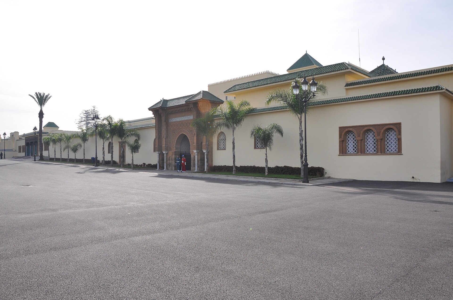 The Royal Palace in Rabat, a cream-walled Moroccan palace with a tiled gate, palm trees and an empty paved square.