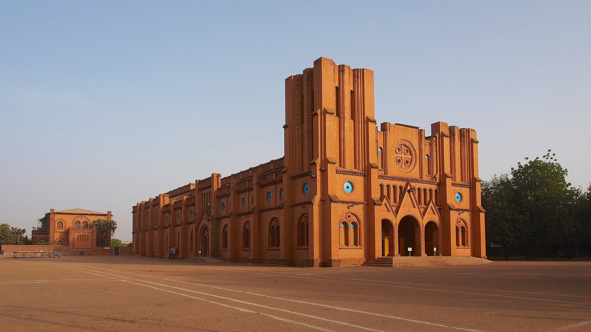 Red brick twin-towered cathedral on an open sandy square in Ouagadougou under a clear sky
