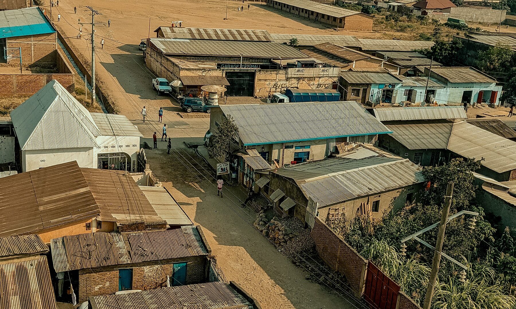 Aerial view of tin-roofed houses and shops along dirt streets, with pedestrians and parked cars, in the Bindoville area of Bujumbura, Burundi.