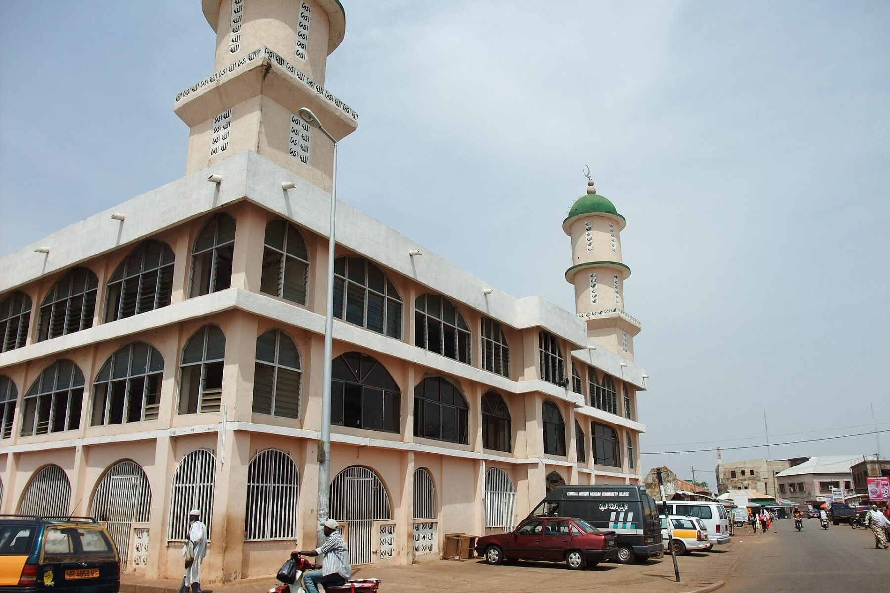 A street corner in Tamale, northern Ghana, with a two-minaret mosque, taxis, a motorcycle and pedestrians