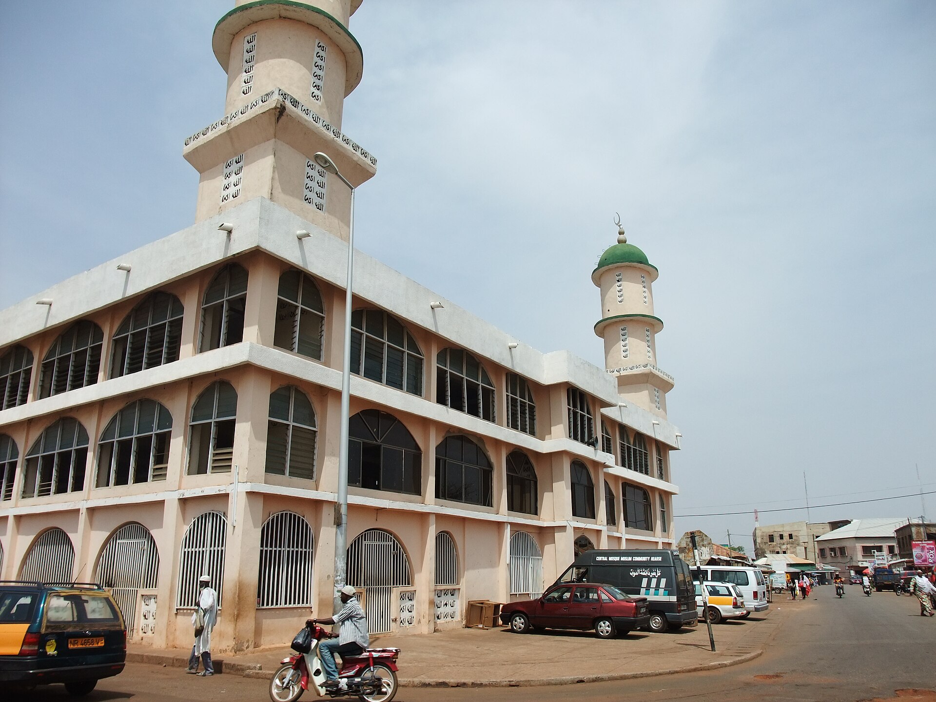 A street corner in Tamale, northern Ghana, with a two-minaret mosque, taxis, a motorcycle and pedestrians