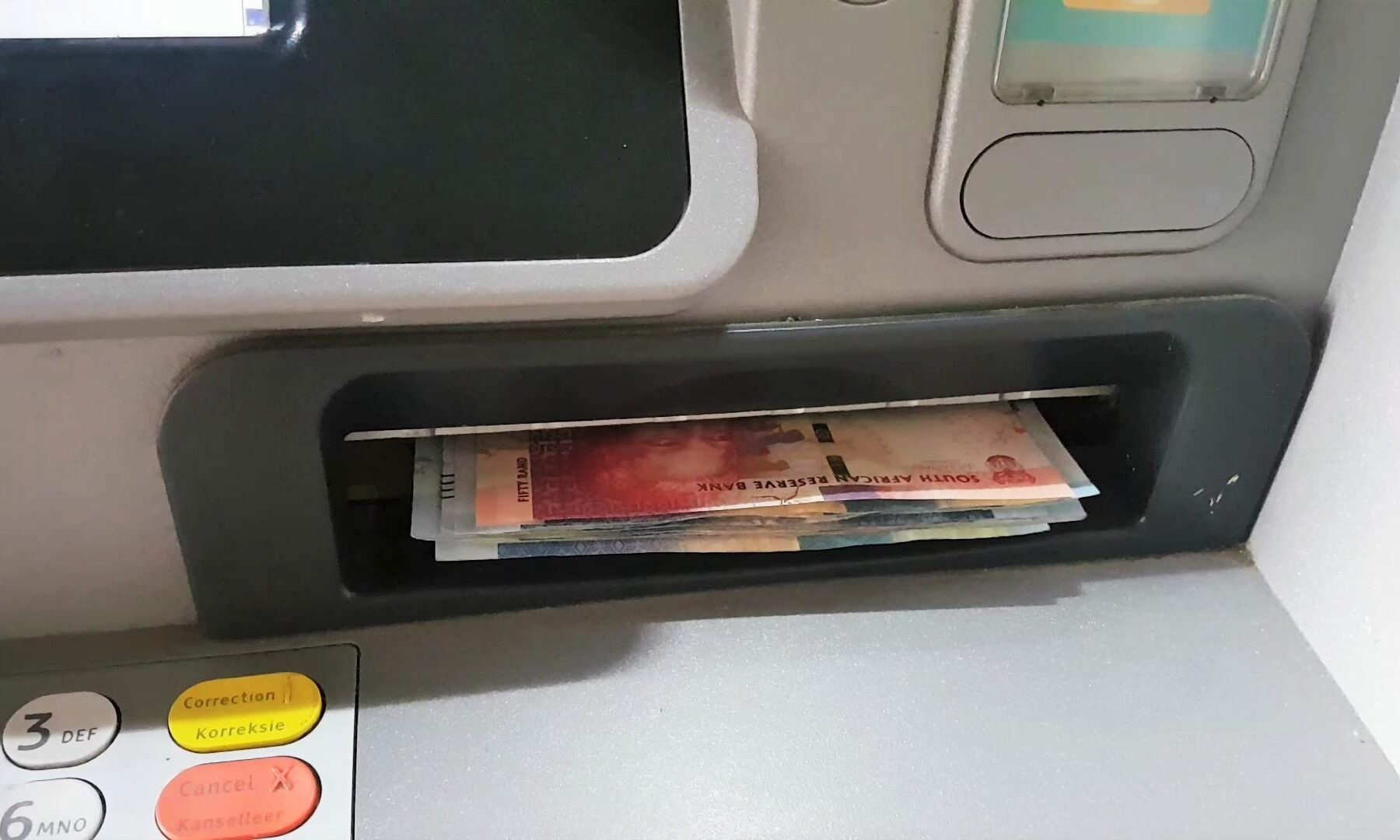 Banknotes in the cash slot of an ATM in South Africa, with part of the keypad visible