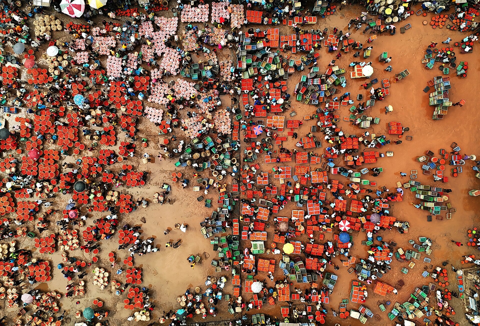Aerial view of a crowded open-air tomato market in Lagos, with traders, red baskets and umbrellas on bare ground