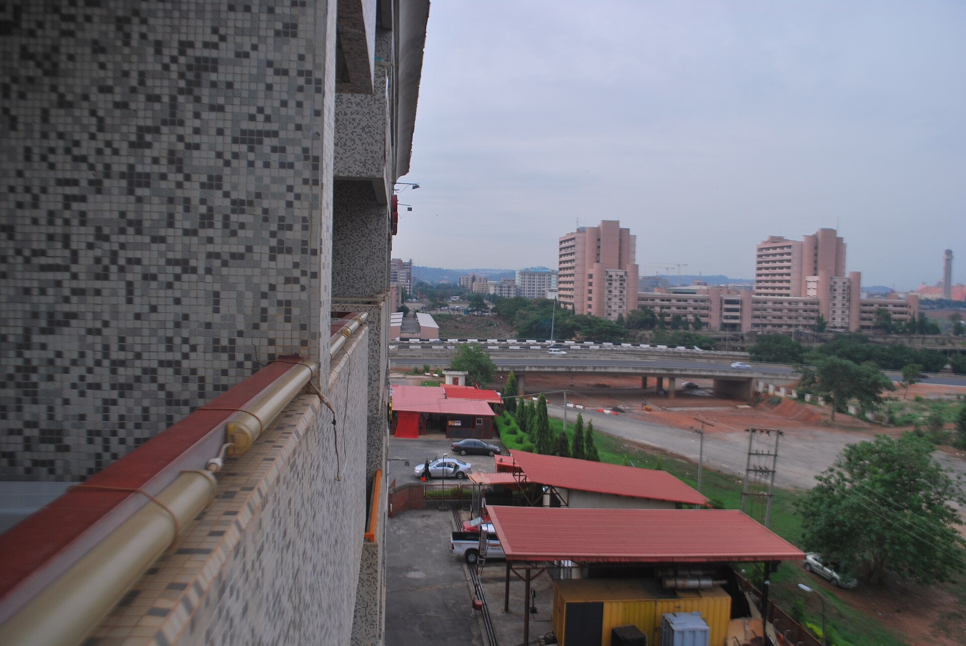 View from a tiled building over central Abuja, Nigeria, with high-rise blocks, red-roofed sheds and an elevated road
