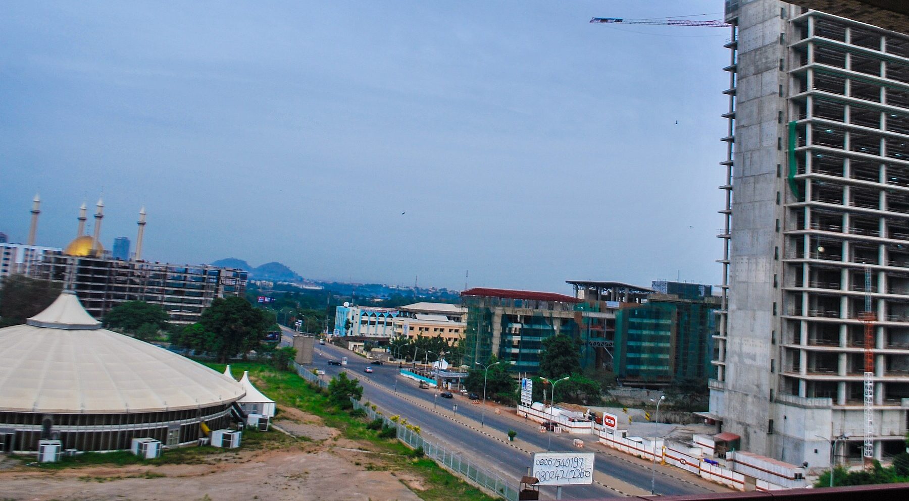 Central district of Abuja with the dome of the National Mosque, a roadside circular hall and a high-rise under construction