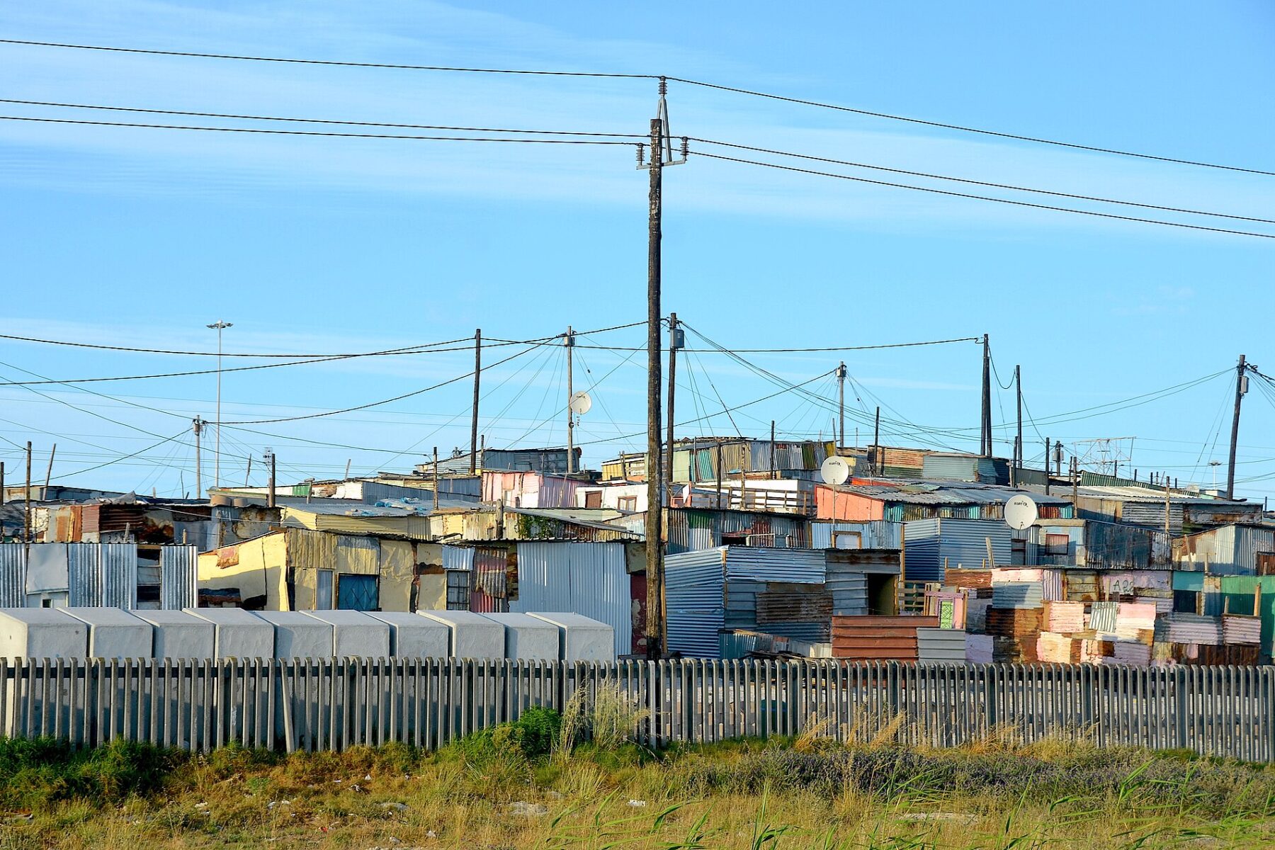 Corrugated iron homes and power lines in Khayelitsha, Cape Town, behind a fence along the N2 road
