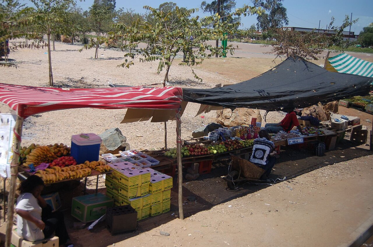 Roadside stalls selling bananas, apples and other fruit under red and black shade cloths in Soweto