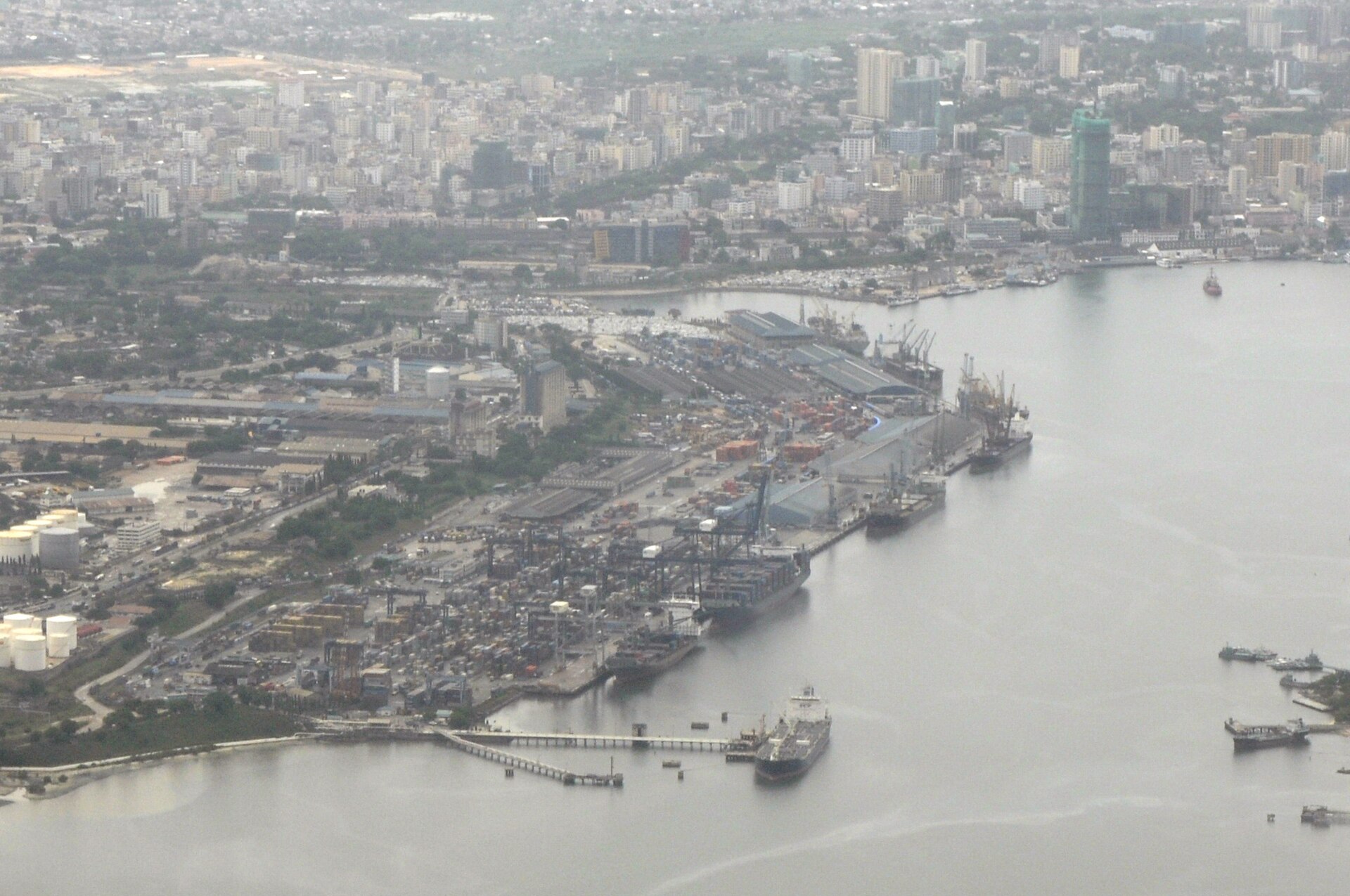Aerial view of the Dar es Salaam harbour with a container terminal, cranes and ships along a quay, and the city skyline behind
