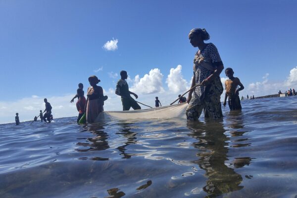 Women and children wade in shallow sea water pulling a fishing net off the coast of a Comoros island.