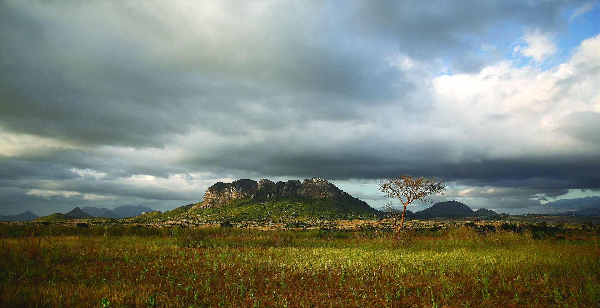 A rocky hill rises from open farmland under heavy storm clouds near Dedza in central Malawi