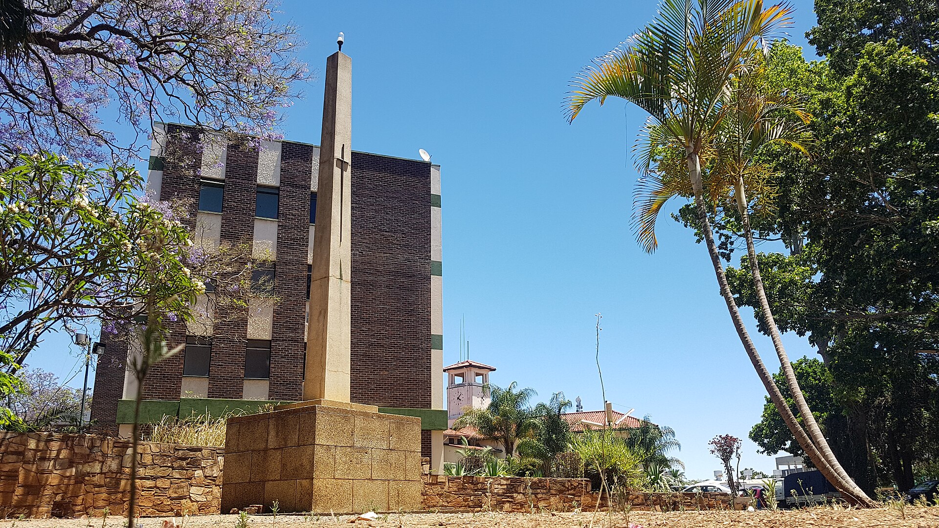 The Gweru Town House building with a stone monument and palm trees under a blue sky.