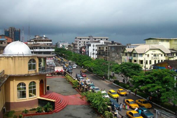 A tree-lined street in central Monrovia with yellow taxis, traffic and low buildings under a dark rain sky