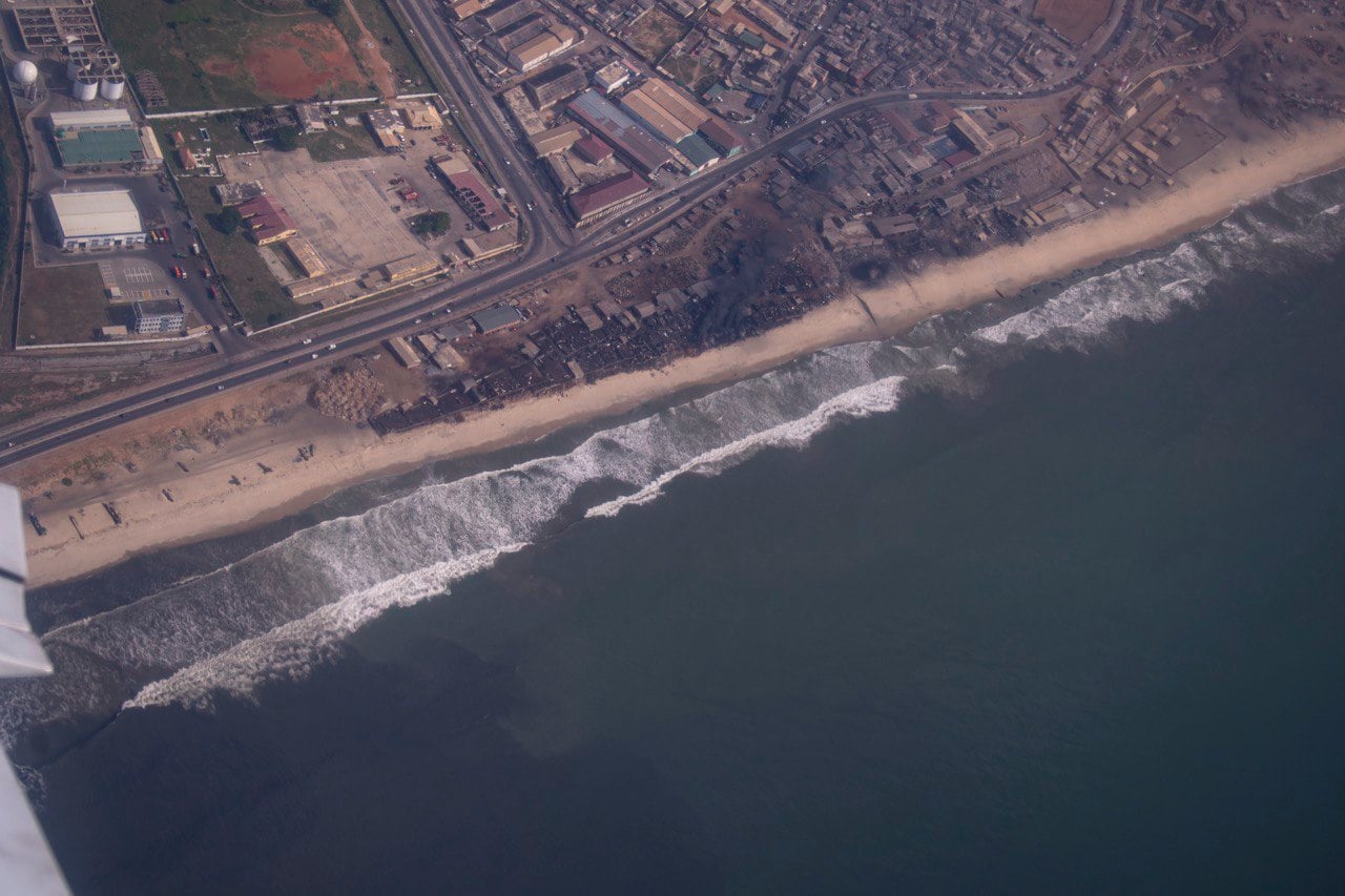 Aerial view of the Accra shoreline with breaking waves, roads, warehouses and dense housing