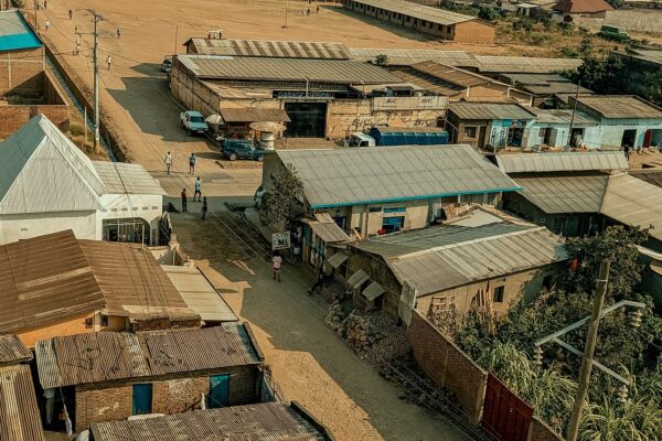 Aerial view of tin-roofed houses and shops along dirt streets, with pedestrians and parked cars, in the Bindoville area of Bujumbura, Burundi.