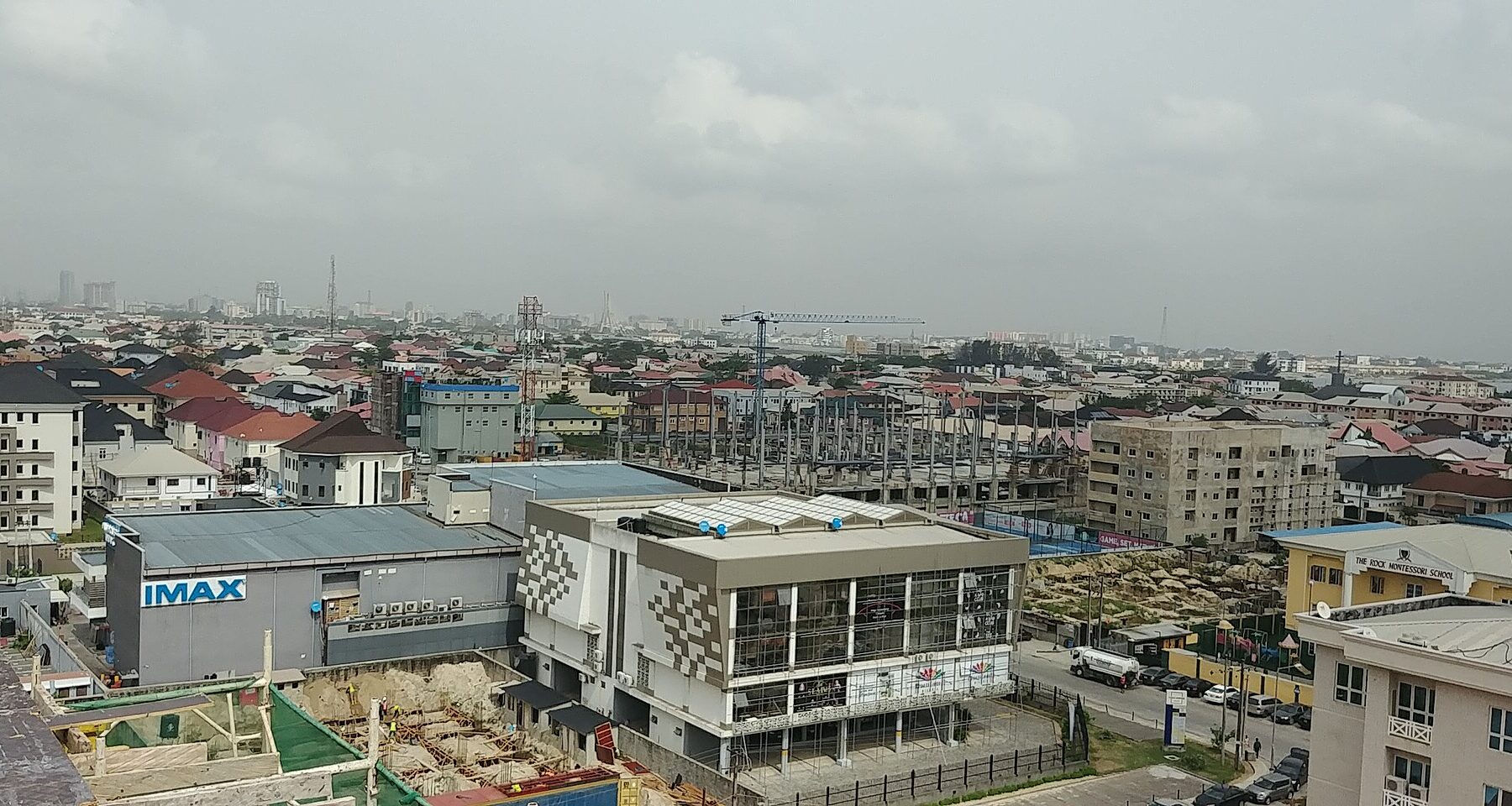 Rooftops of Lekki Phase 1 in Lagos with a cinema building bearing an IMAX sign at left and the city skyline on the hazy horizon