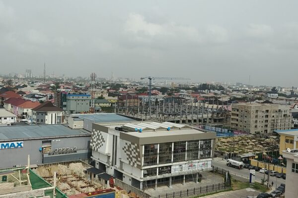 Rooftops of Lekki Phase 1 in Lagos with a cinema building bearing an IMAX sign at left and the city skyline on the hazy horizon