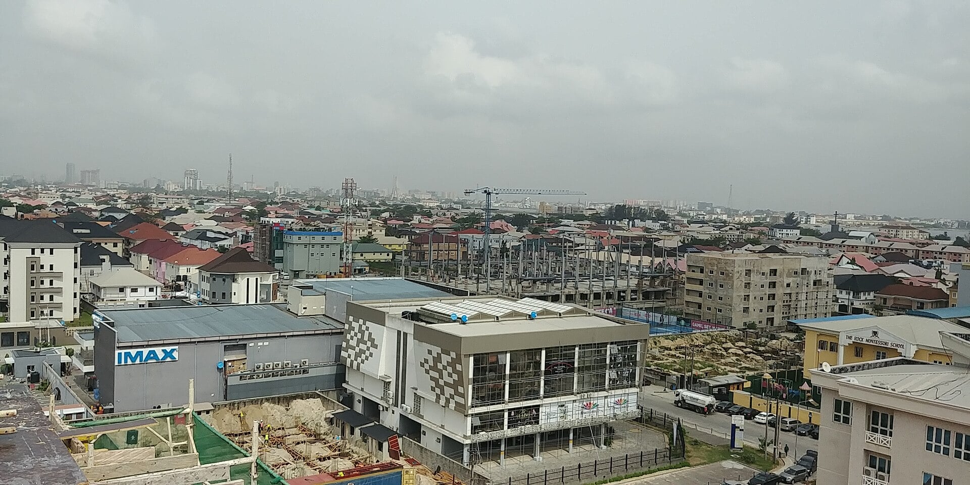 Rooftops of Lekki Phase 1 in Lagos with a cinema building bearing an IMAX sign at left and the city skyline on the hazy horizon