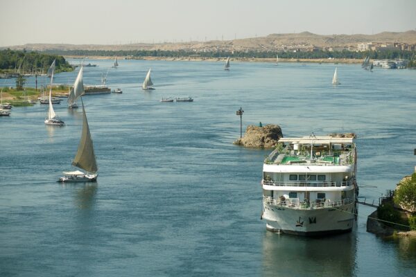 A white river cruise boat and several sailing feluccas on the Nile at Aswan with desert hills behind