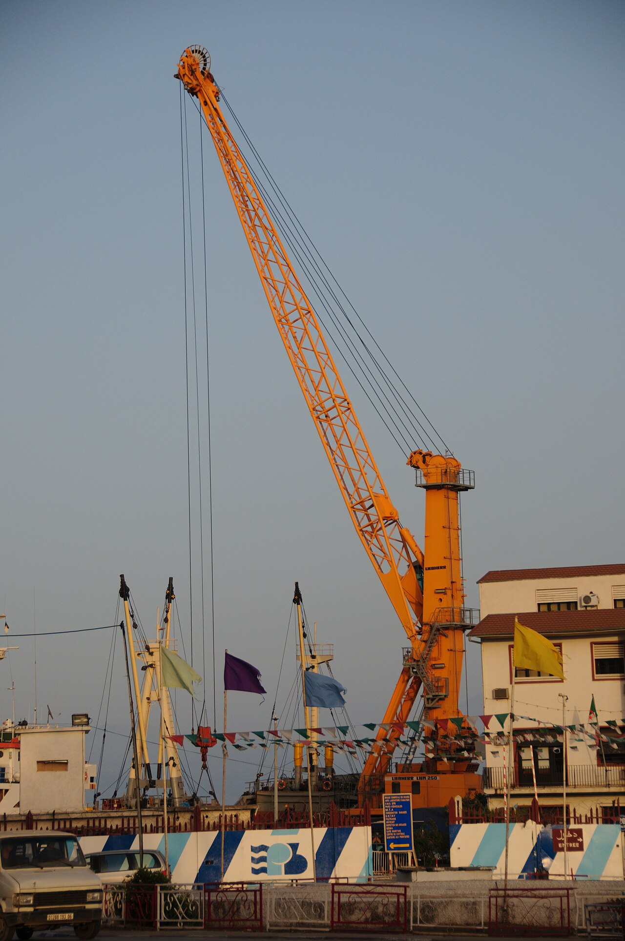 A yellow port crane and fishing boats at the harbour of Béjaïa, an Algerian Mediterranean port