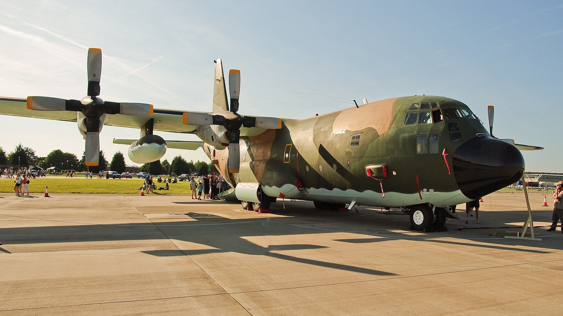An Algerian Air Force Lockheed C-130H Hercules transport with olive and tan camouflage parked on an apron at an air show