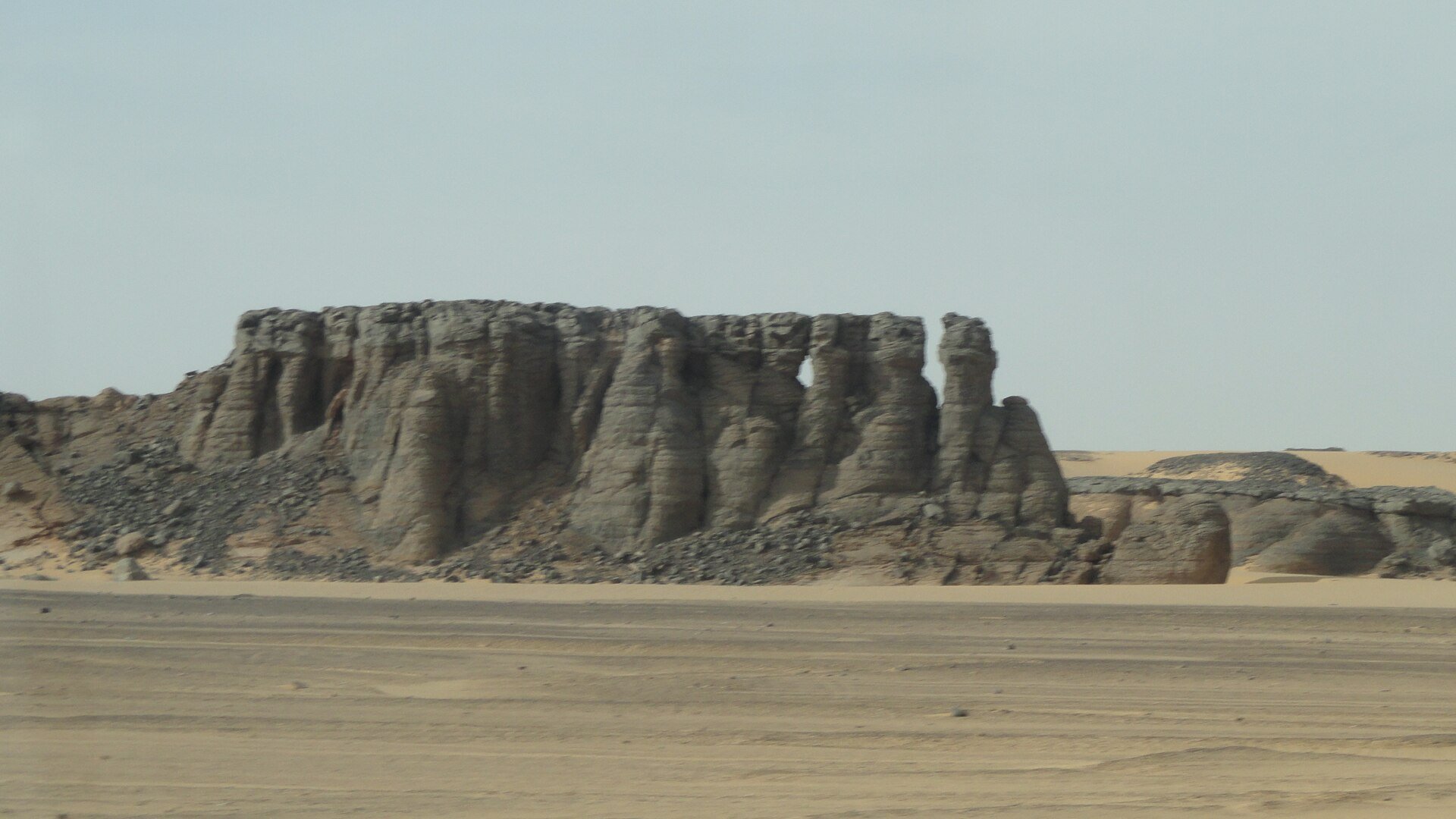 A rock outcrop and sand plain in the Algerian Sahara, filed under In Guezzam, a town near the border with Niger