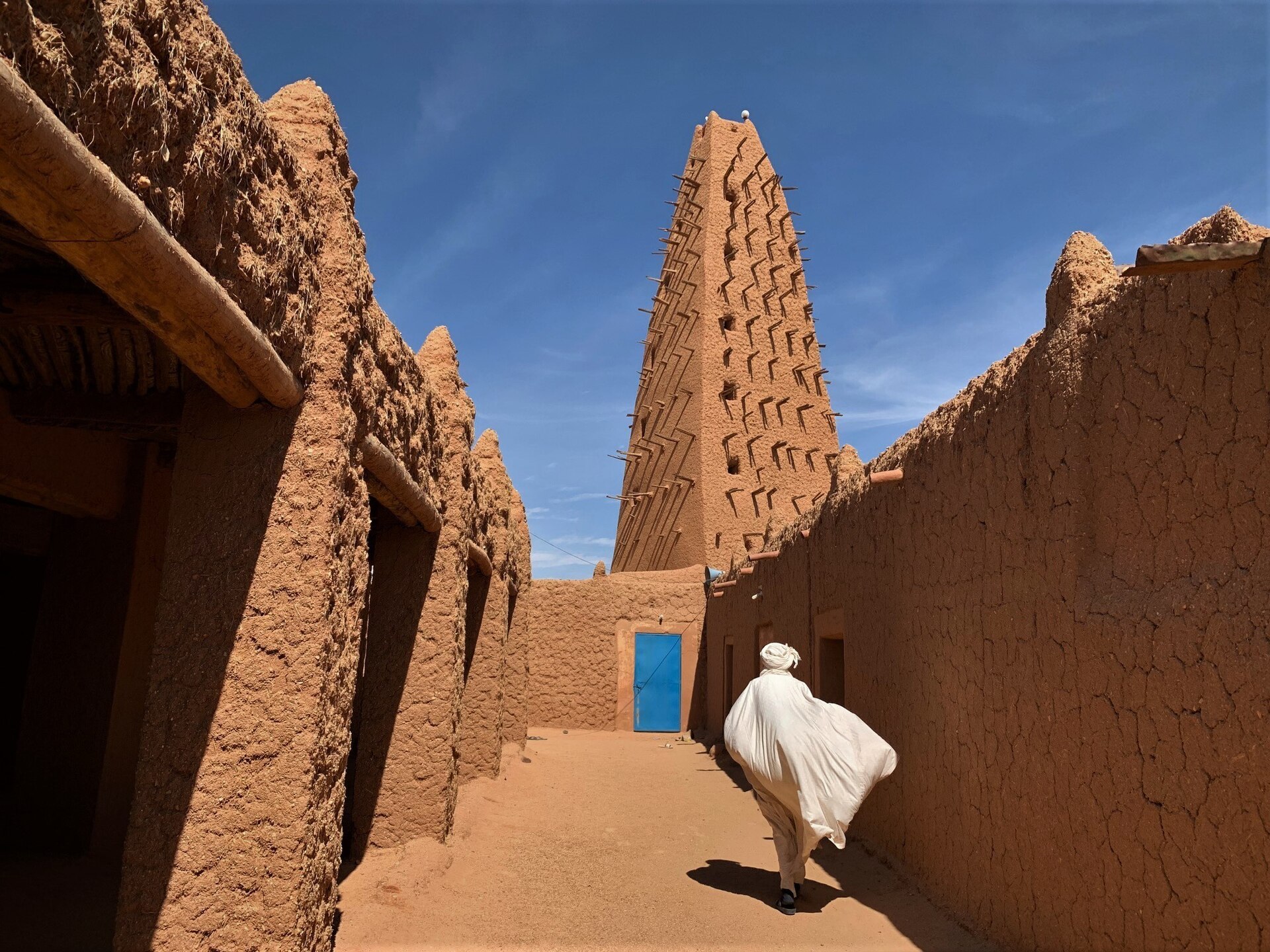 Mud-brick minaret of the Grand Mosque of Agadez in northern Niger, with a man in a white robe walking down a sand-coloured lane