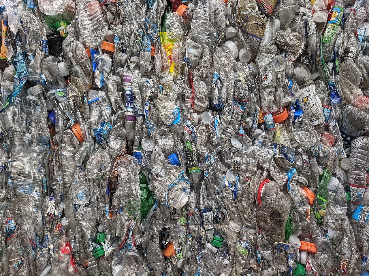 Close-up of crushed clear PET plastic bottles and coloured caps pressed into one bale