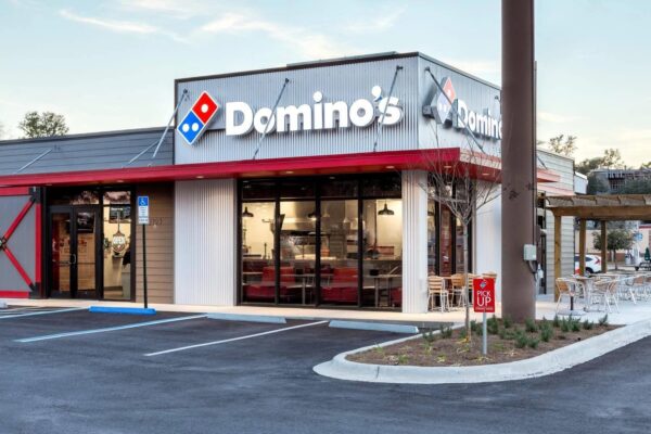 A Domino's pizza restaurant with a lit red and blue logo at dusk