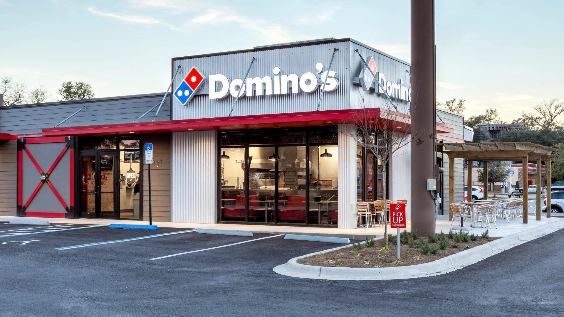 A Domino's pizza restaurant with a lit red and blue logo at dusk