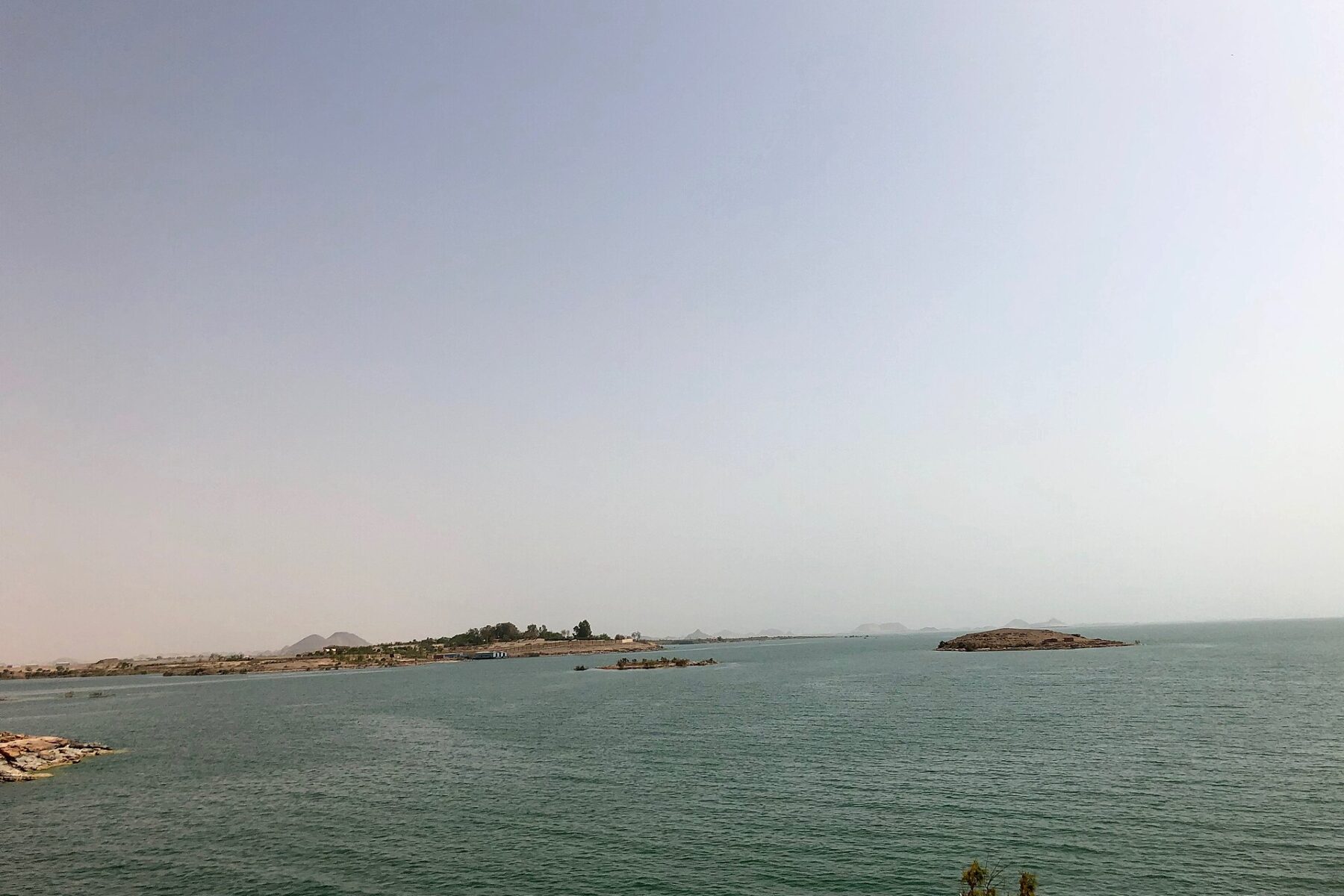 Green water of Lake Nasser under a hazy sky, with low islands and a distant shore near Abu Simbel in southern Egypt