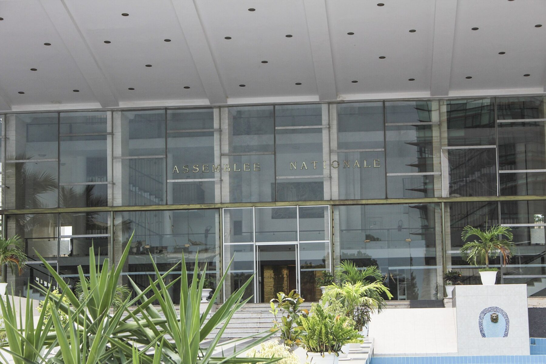 Glass facade of the National Assembly building in Dakar with the words Assemblee Nationale above the entrance and palm plants in front