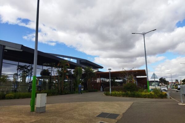 Glass and timber passenger terminal at Antananarivo airport with palm plants, street lamps and a bus under a cloudy sky