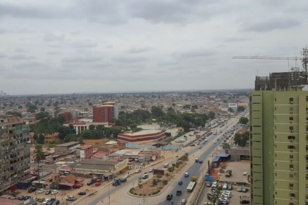 A busy road through the Rangel district of Luanda with apartment blocks and a construction crane