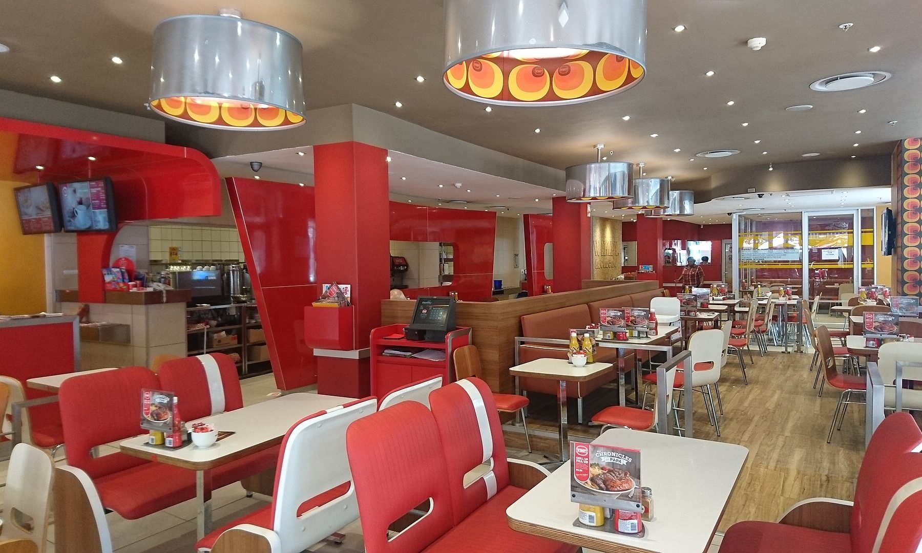 Red and white diner-style restaurant interior with booths, tables and round orange-patterned ceiling lamps