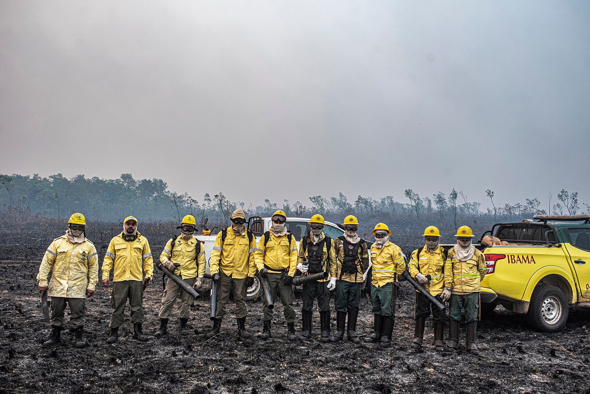 Ten Ibama Prevfogo brigade members in yellow gear stand on burned ground under heavy smoke in the Tenharim Marmelos Indigenous Land, Amazonas, Brazil