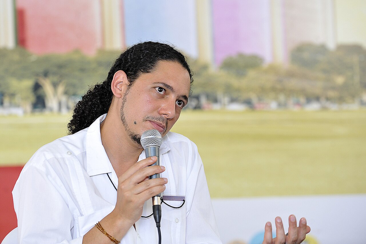 The Angolan writer Ondjaki holds a microphone and listens to a question at a book event in Brasília.