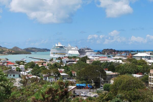 View over downtown St. John's, the capital of Antigua and Barbuda, with cruise ships at the harbour pier and green hills beyond.