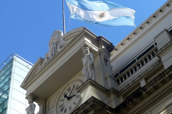 Argentine flag flying above the clock and sculptures of the central bank headquarters in Buenos Aires under a blue sky
