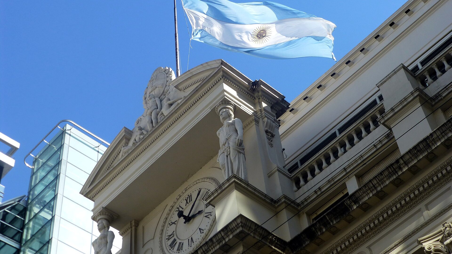 Argentine flag flying above the clock and facade of the central bank headquarters in Buenos Aires