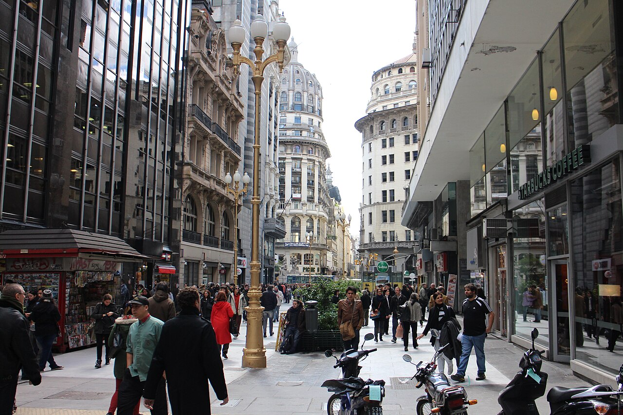 Crowded pedestrian Calle Florida in central Buenos Aires with ornate lamp posts, a newsstand, shops and domed buildings