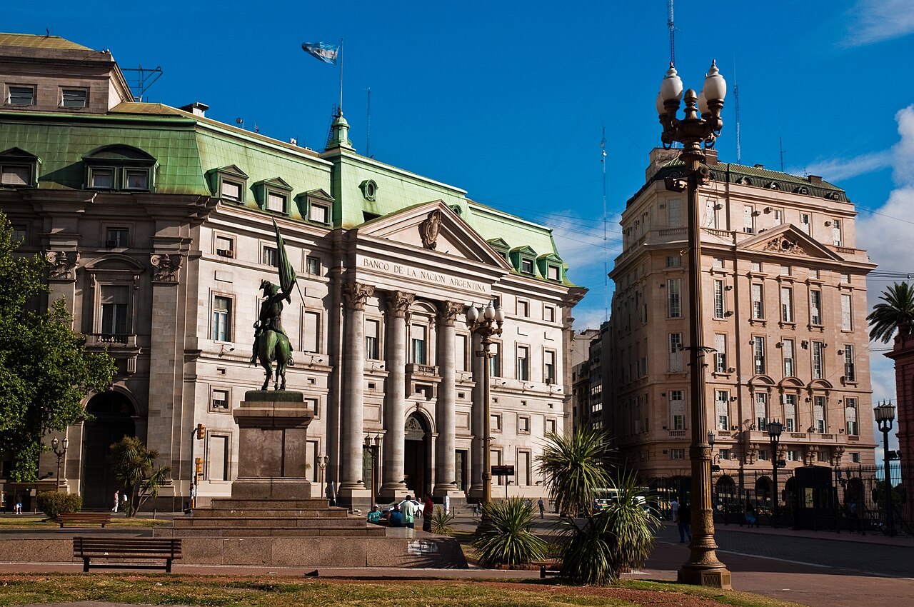 Stone facade of the Banco de la Nación Argentina head office with a green roof, an equestrian statue and a street lamp in front