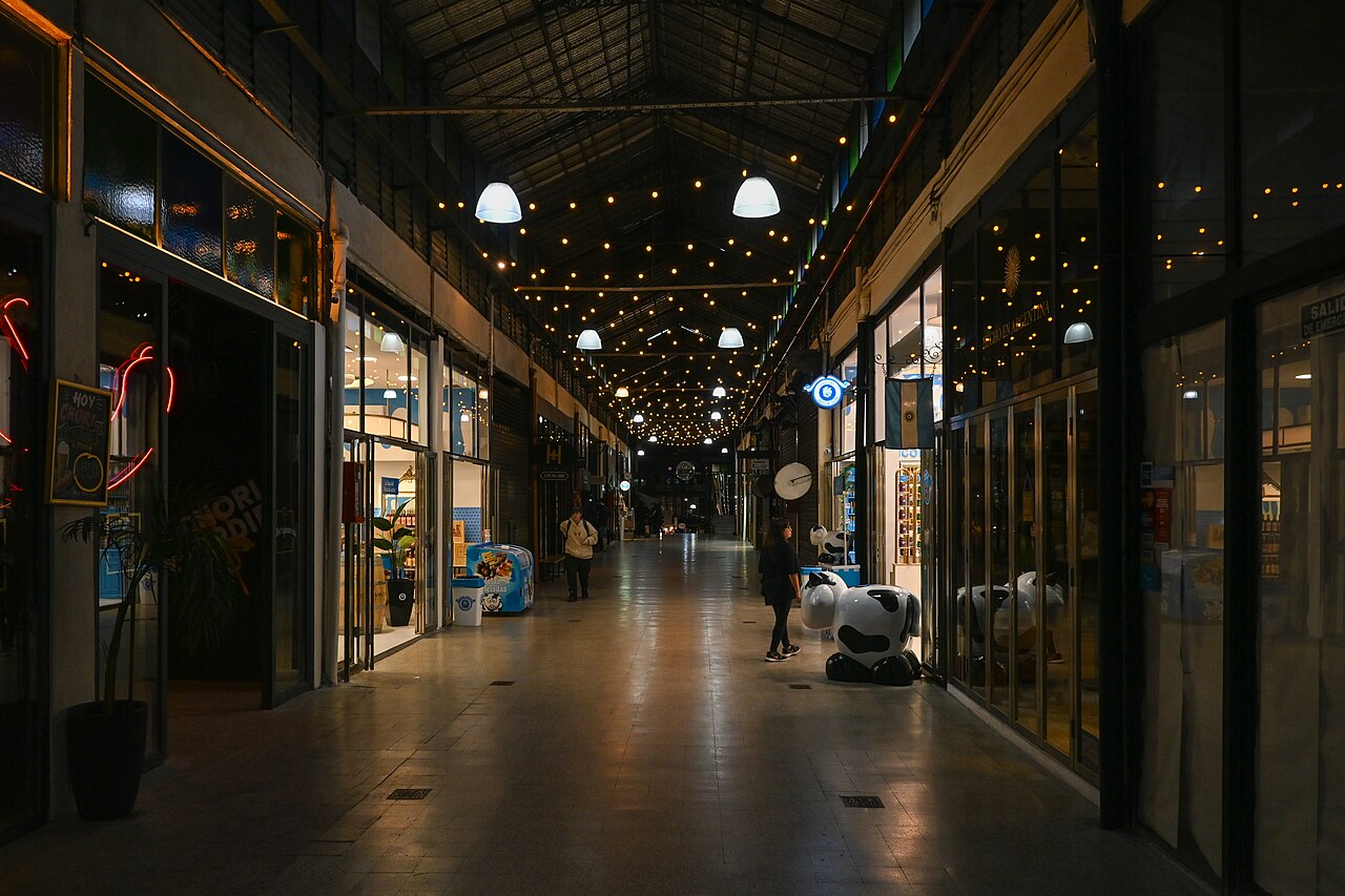 Covered gallery inside the San Telmo Market in Buenos Aires with lit shopfronts, string lights and a few shoppers