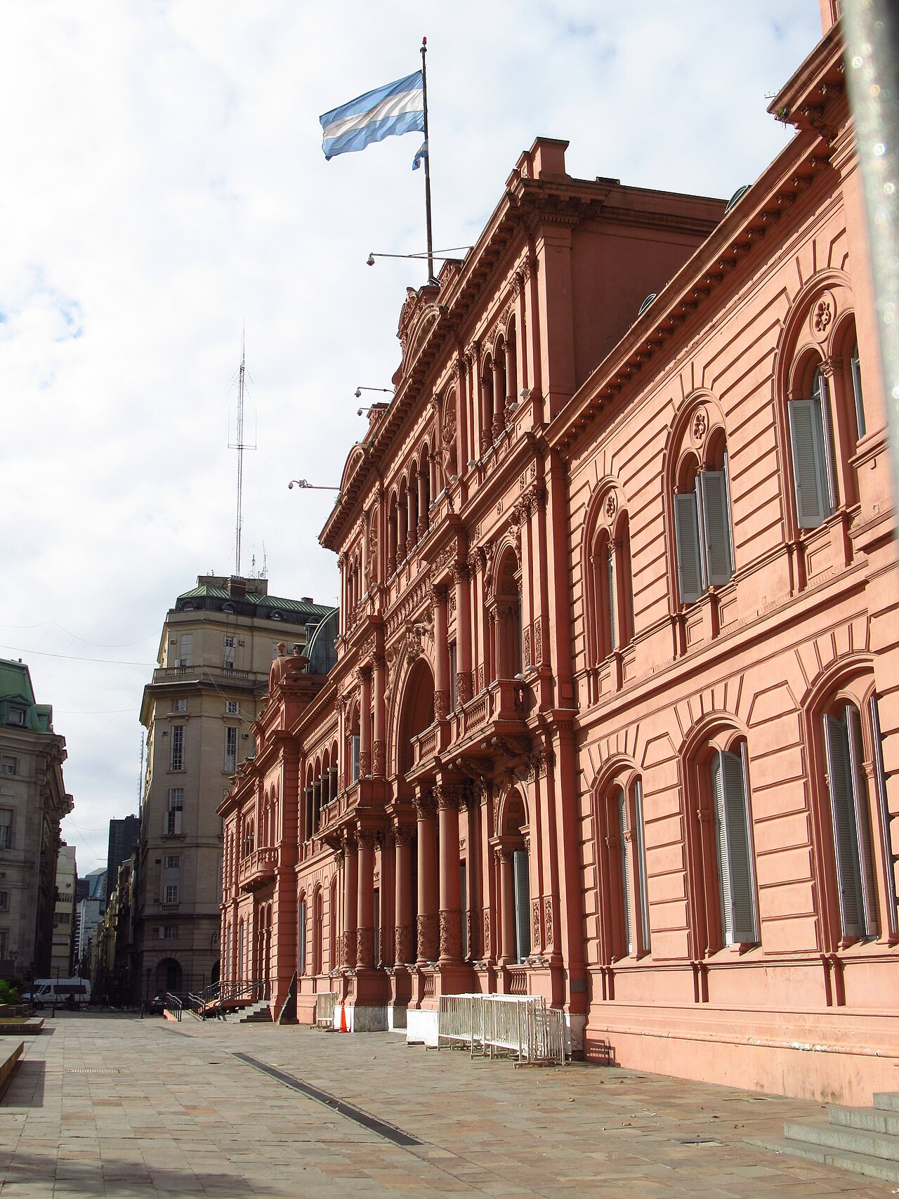 Pink facade of the Casa Rosada beside a paved plaza in Buenos Aires, with the Argentine flag on the roof