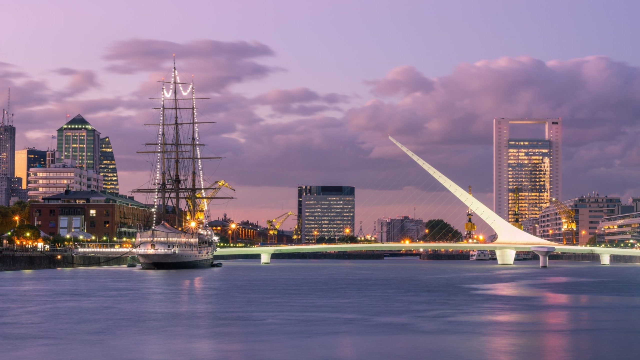Puerto Madero waterfront in Buenos Aires at dusk, with the Puente de la Mujer footbridge and a moored tall ship