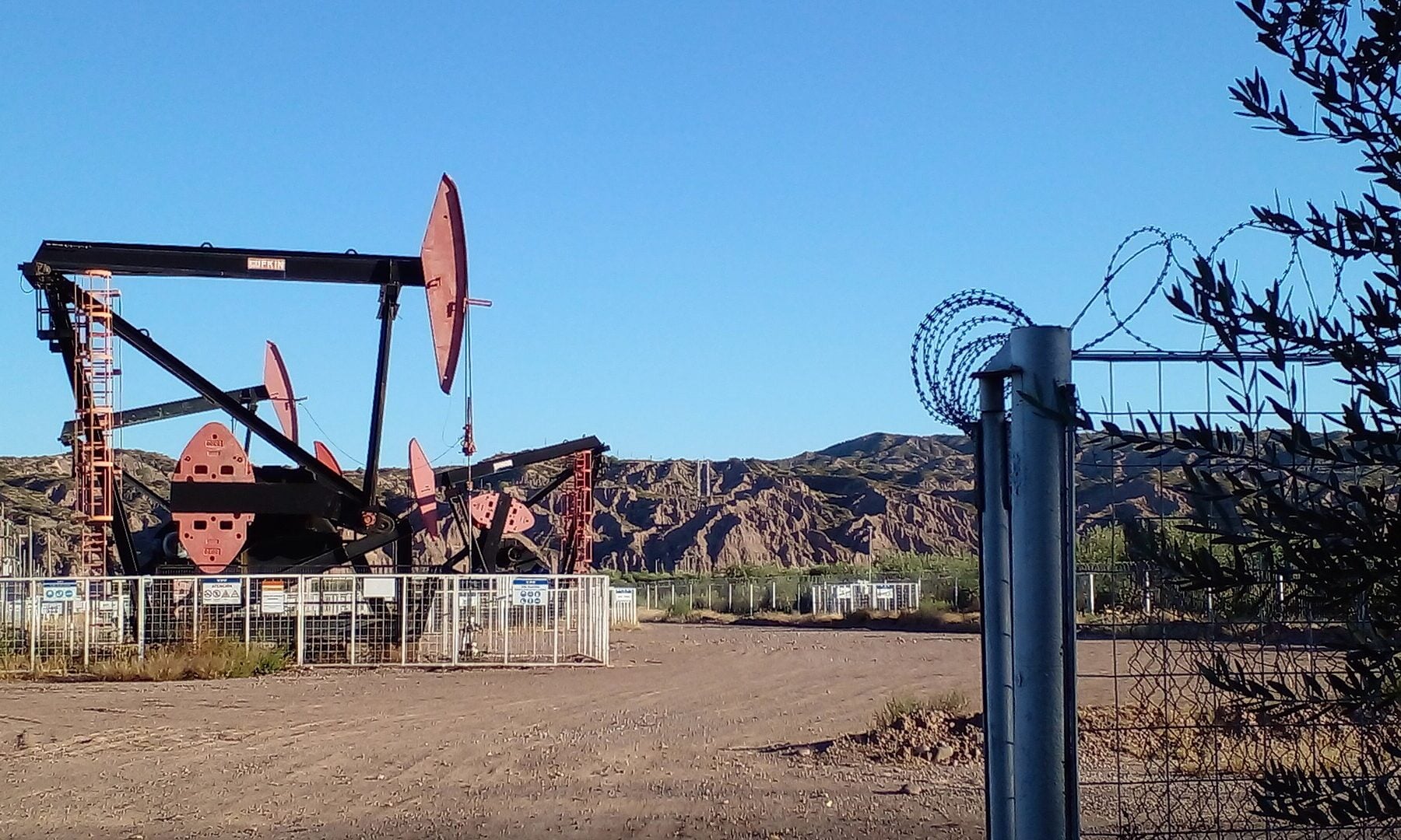 Oil pumpjacks behind a fence at Lunlunta in Mendoza province, Argentina, with barren hills and a clear blue sky, for the YPF stock and inflation story