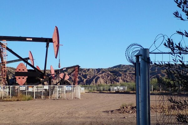 Oil pumpjacks behind a fence at Lunlunta in Mendoza province, Argentina, with barren hills and a clear blue sky, for the YPF stock and inflation story