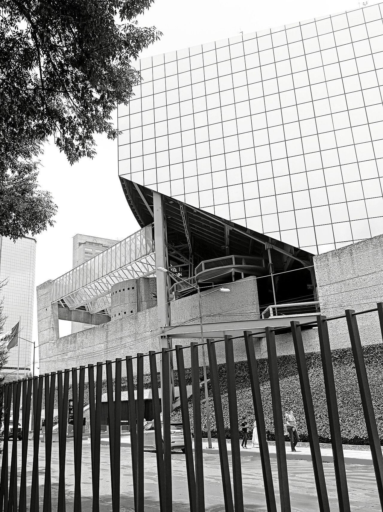 Black-and-white side view of the Auditorio Nacional in Mexico City, with a glass-covered walkway behind a fence.