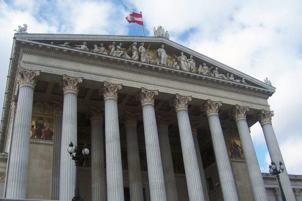 The Austrian Parliament Building in Vienna with its white columns and a red-white-red flag above the pediment