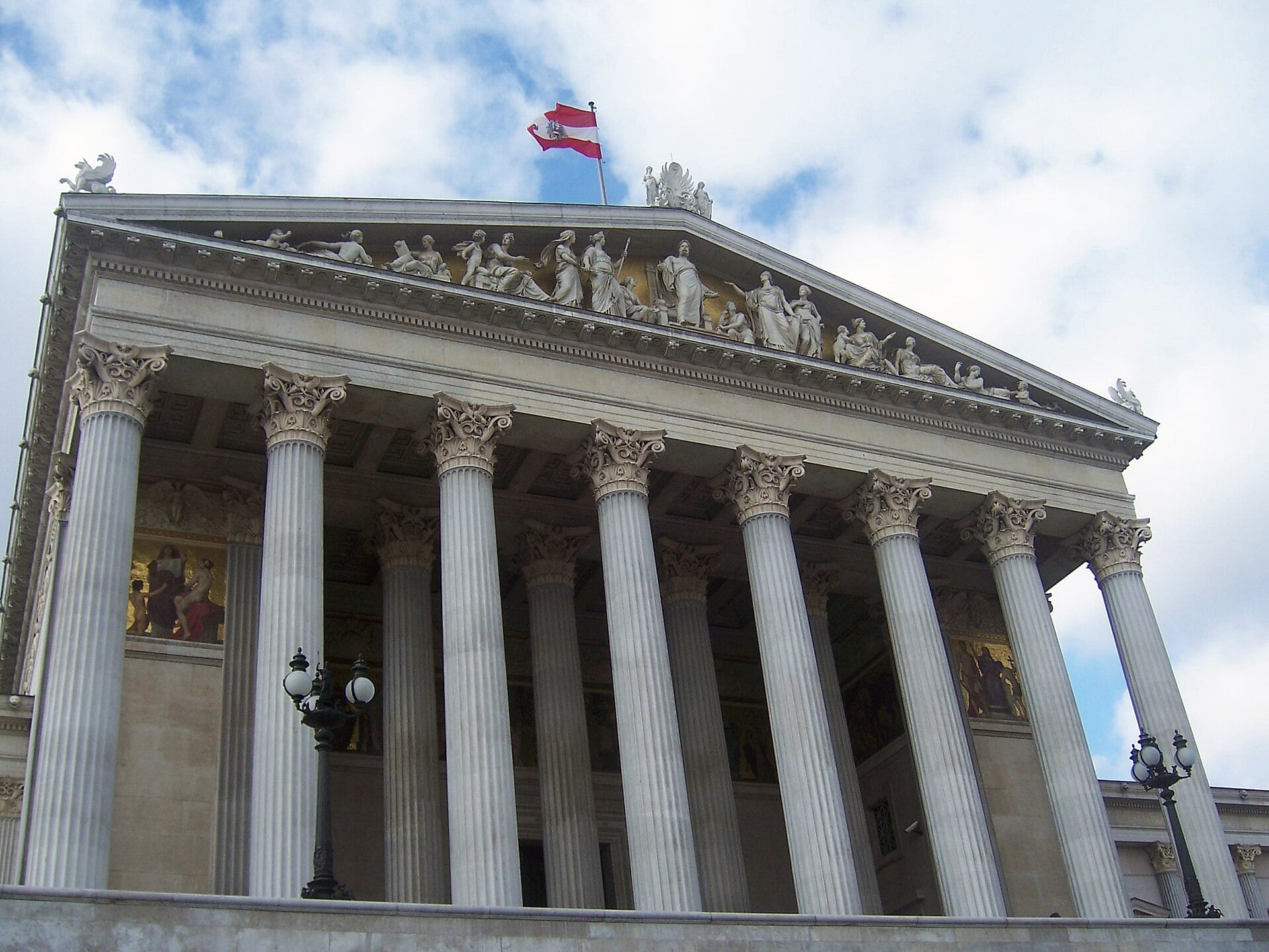 The Austrian Parliament Building in Vienna with its white columns and a red-white-red flag above the pediment