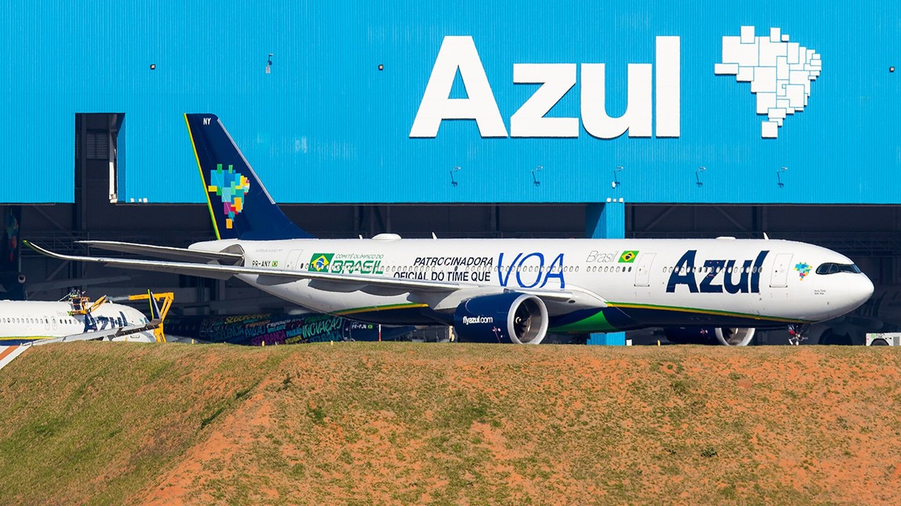 Azul Airbus A330-900 in a special livery parked in front of the airline's blue hangar with its logo, with a grassy embankment in the foreground